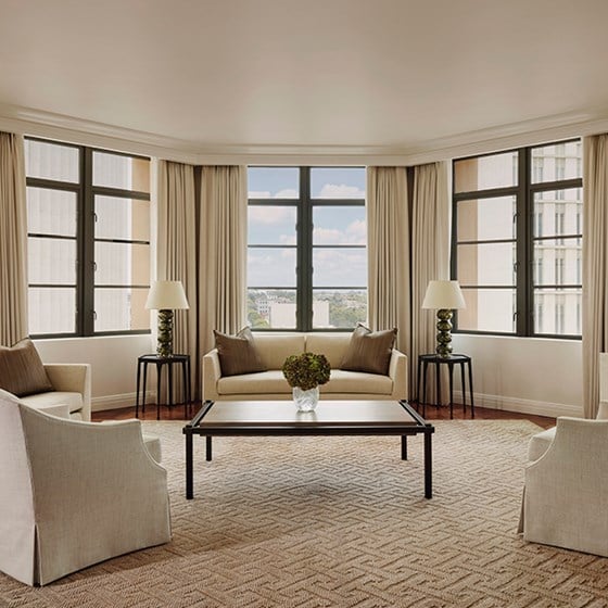 A hexagon shaped living room with white couches and sitting chairs. The walls are large, floor to ceiling windows.