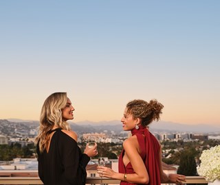 Two women sipping champagne on an outdoor balcony overlooking Beverly Hills during sunset