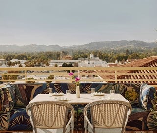 An outside table with a pink flower in a vase at a restaurant overlooking a city skyline with rolling hills and buildings.
