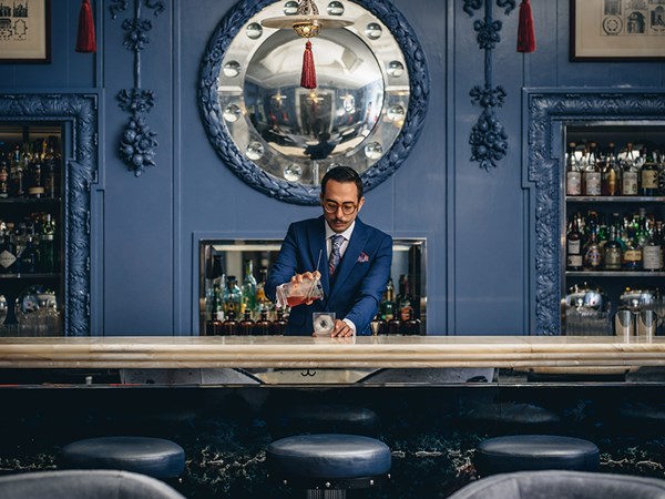A bartender in a suit in a blue bar mixing a cocktail.