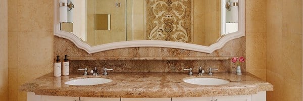 A brown marble sink top with white drawers. In the mirror a shower can be seen with a tiled mosaic wall.
