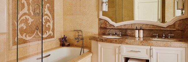 A tiled bathroom, a bathtub with a tiled wall mosaic, and a brown marble sink with white drawers.