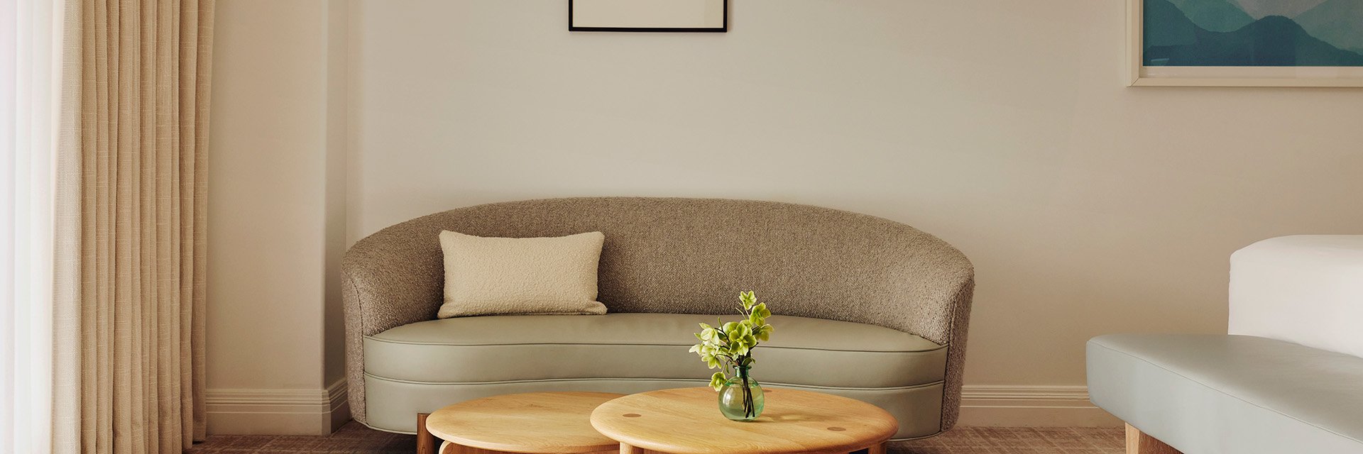A curved ivory couch with a small, white pillow. A potted green plant sitting on a wooden coffee table.