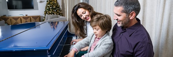 Family sitting at a blue piano with a christmas tree in the background