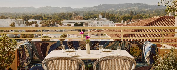 An outside table with a pink flower in a vase at a restaurant overlooking a city skyline with rolling hills and buildings.