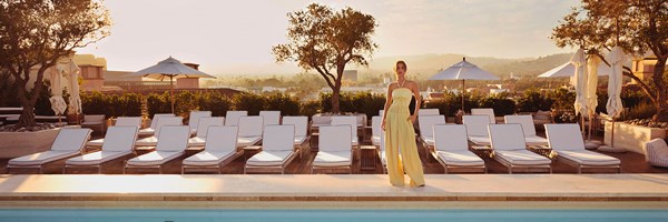 A woman in a yellow dress standing by a rooftop pool during golden hour.