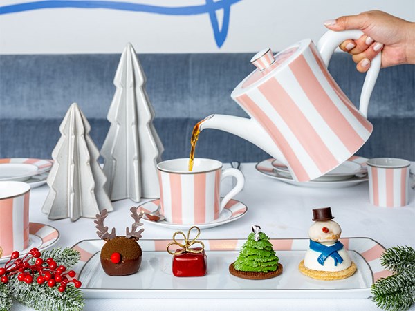 A whimsical tea setting with pink-striped teapot and cups, surrounded by holiday-themed pastries shaped as reindeer, Christmas tree, gift box, and snowman.