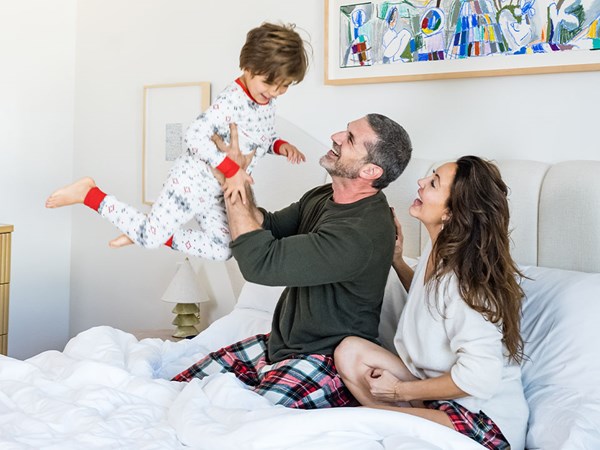 A cozy family moment in bed with parents joyfully playing with a child in holiday pajamas, capturing warmth and togetherness.