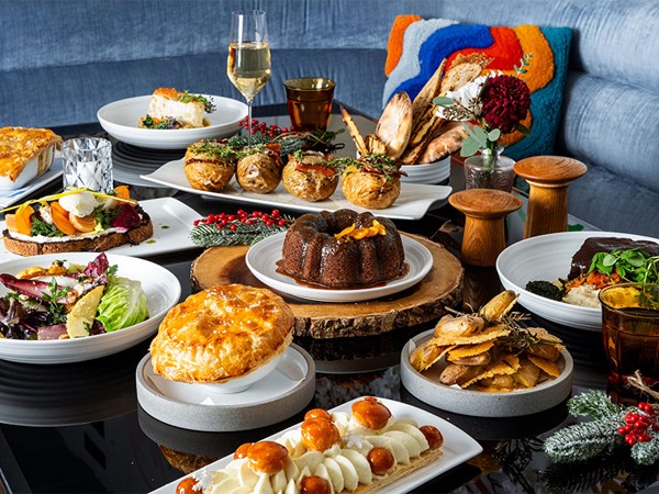 An elegantly arranged holiday meal with various gourmet dishes, including pastries, salads, and desserts, set on a table with festive decor and sparkling beverages.